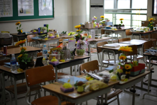 The space is filled to the brim with flowers, cards, and offerings. The chalkboard tells stories of grief, shock, and loss.