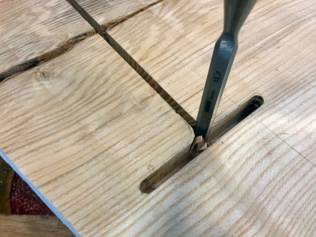 He chiseled out a space at the end of the table on a part where the wood had split. The leg would prevent further damage after it was in place.
