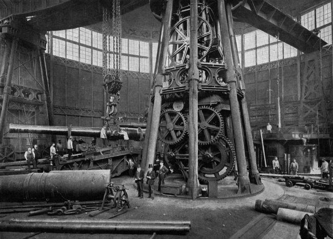 Workers use a steam crane to lower this breech-loading gun into place. 