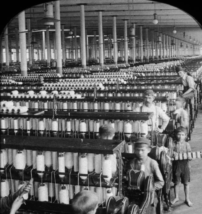 Child workers are supervised by an adult while working in a spinning factory.