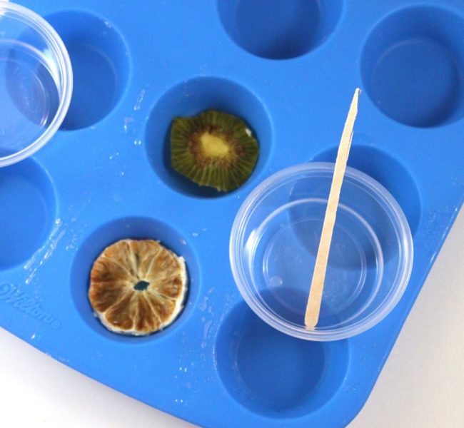 Using a silicone cupcake pan, rawdesignco adds the resin to the fruit slices.  She moves the slices around in the mixture using popsicle sticks.