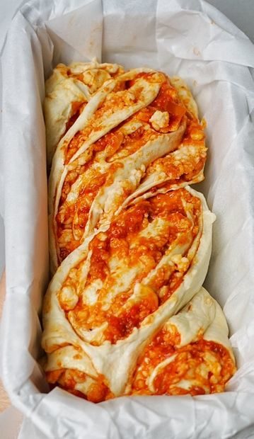Now for the fun part -- twist the two rolls together, top with extra cheese, sauce, and pepperoni, and place them in a parchment paper-lined pan for baking.