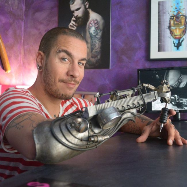 Gonzal decided to mount a tattoo machine onto an existing prosthetic arm and give it to Tenet.  He also added parts from a mechanical typewriter and a gramophone, then painted it for a rusty appearance.