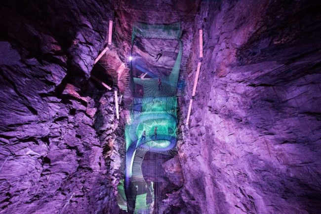 Giant net trampolines are suspended above the cave floor with neon lights brightening up the space.